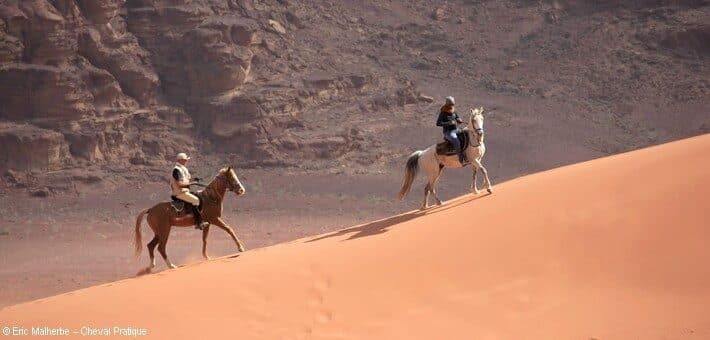 Deux cavaliers gravissent une dune de sable rouge dans le désert du Wadi Rum